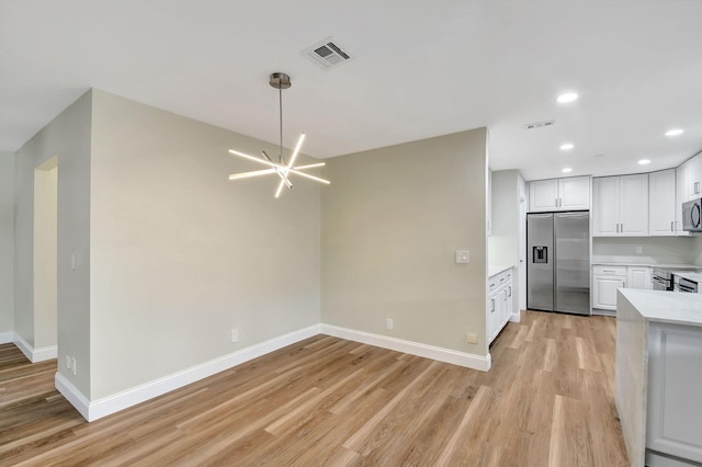 kitchen with stainless steel appliances, an inviting chandelier, white cabinets, and light hardwood / wood-style floors