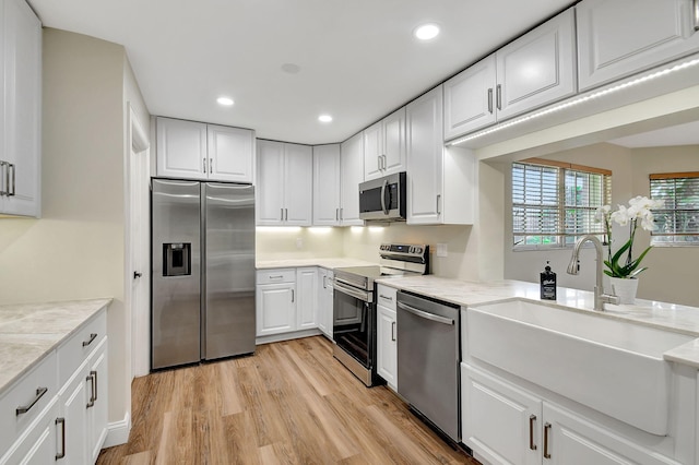 kitchen with sink, light stone counters, light wood-type flooring, appliances with stainless steel finishes, and white cabinets