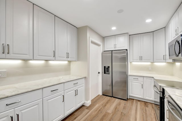 kitchen featuring white cabinetry, stainless steel appliances, light stone countertops, and light hardwood / wood-style floors