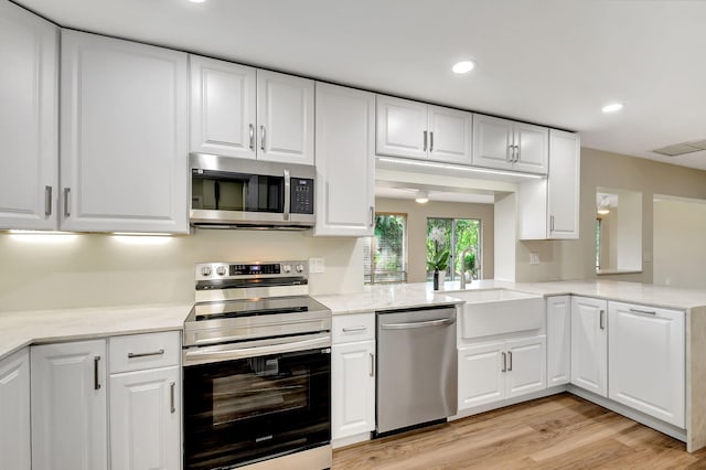 kitchen with sink, light wood-type flooring, appliances with stainless steel finishes, kitchen peninsula, and white cabinets