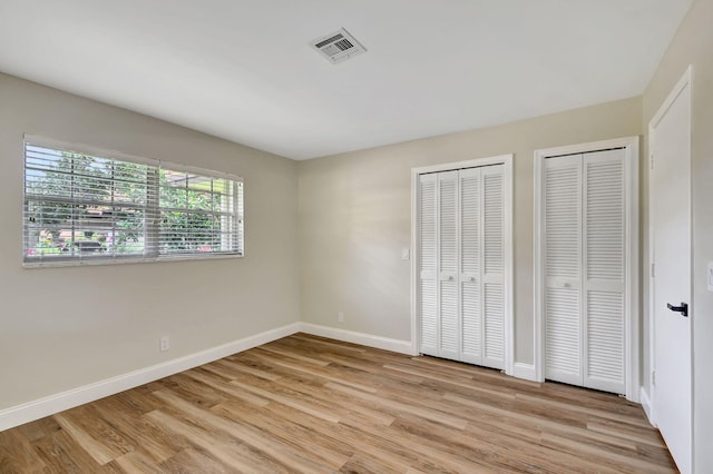 unfurnished bedroom with multiple closets and light hardwood / wood-style floors