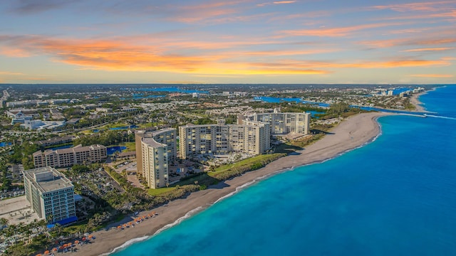 aerial view at dusk featuring a view of the beach and a water view