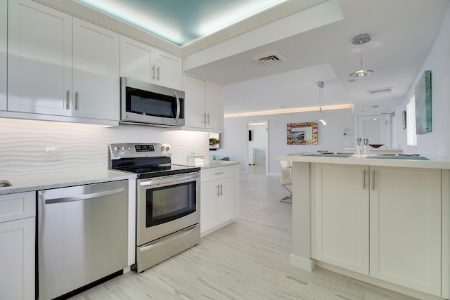 kitchen with white cabinets, decorative backsplash, stainless steel appliances, and decorative light fixtures