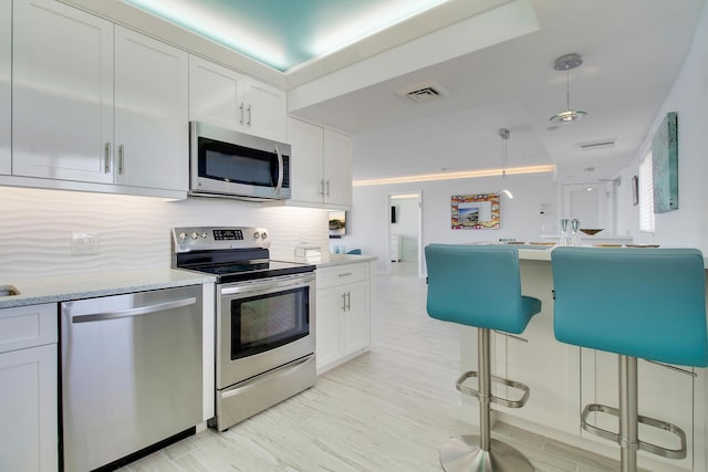 kitchen featuring backsplash, white cabinets, pendant lighting, and appliances with stainless steel finishes