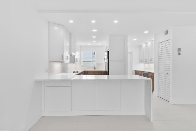 kitchen featuring stainless steel fridge, kitchen peninsula, and white cabinetry