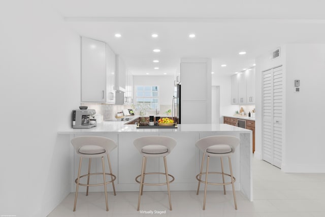 kitchen featuring kitchen peninsula, stainless steel fridge, backsplash, a breakfast bar, and white cabinets