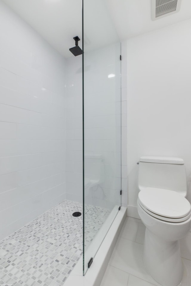 bathroom featuring toilet, a tile shower, and tile patterned floors