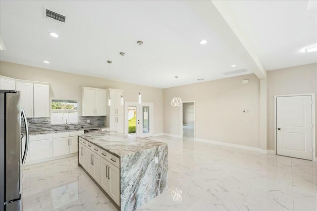 kitchen featuring white cabinets, hanging light fixtures, stainless steel fridge, light stone countertops, and a kitchen island