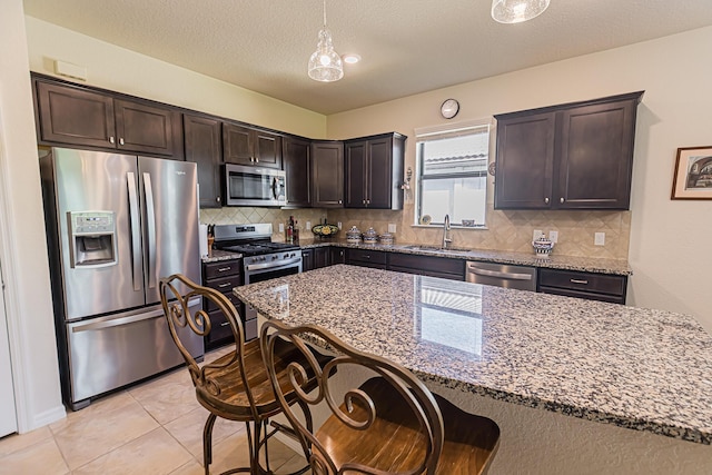 kitchen with pendant lighting, sink, stainless steel appliances, light stone countertops, and dark brown cabinets