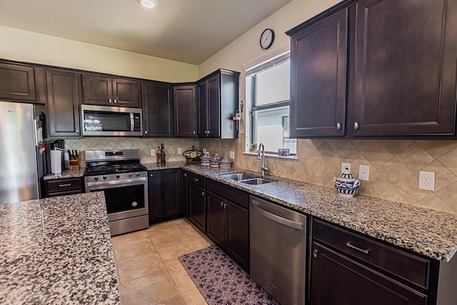 kitchen featuring sink, dark brown cabinets, dark stone countertops, appliances with stainless steel finishes, and decorative backsplash