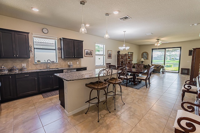 kitchen with a kitchen bar, sink, decorative light fixtures, a kitchen island, and light stone countertops