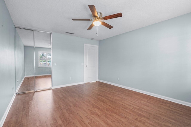 unfurnished bedroom with ceiling fan, a closet, a textured ceiling, and hardwood / wood-style flooring