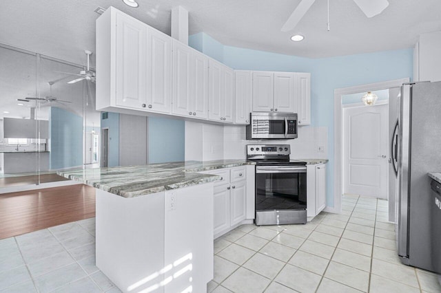 kitchen featuring kitchen peninsula, appliances with stainless steel finishes, dark stone countertops, light hardwood / wood-style floors, and white cabinetry