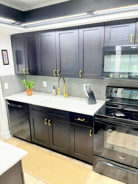 kitchen with decorative backsplash, sink, black appliances, and light hardwood / wood-style floors