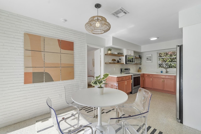 kitchen with backsplash, brick wall, stainless steel appliances, sink, and hanging light fixtures