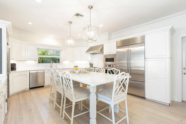 kitchen with light wood-type flooring, stainless steel appliances, a kitchen island, and wall chimney range hood