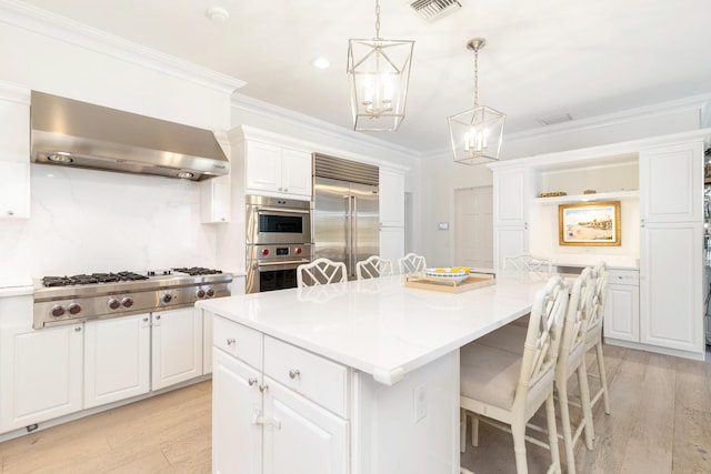 kitchen with appliances with stainless steel finishes, light wood-type flooring, wall chimney range hood, a center island, and a breakfast bar area