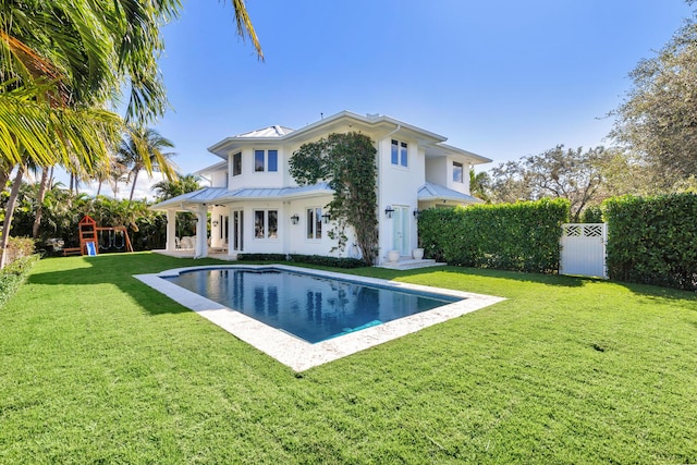 rear view of house with a fenced in pool, a playground, and a lawn