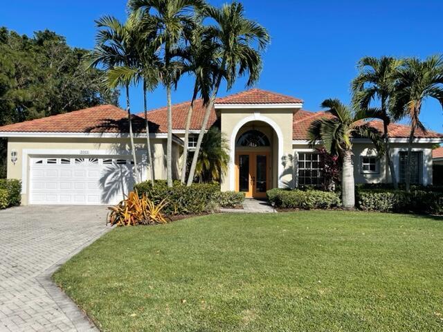 mediterranean / spanish-style house with french doors, decorative driveway, stucco siding, a garage, and a front lawn