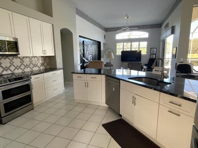 kitchen featuring light tile patterned floors, a sink, open floor plan, appliances with stainless steel finishes, and tasteful backsplash