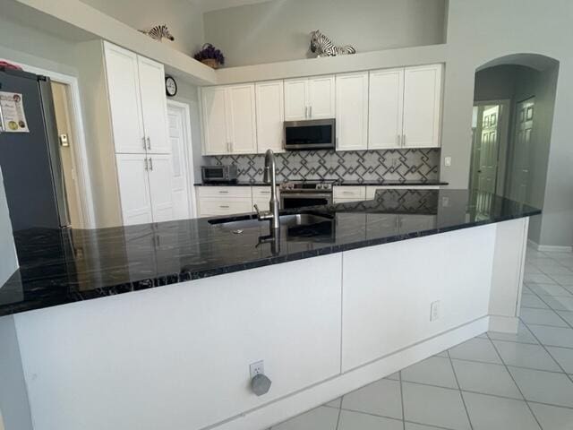 kitchen featuring tasteful backsplash, arched walkways, appliances with stainless steel finishes, white cabinetry, and a sink