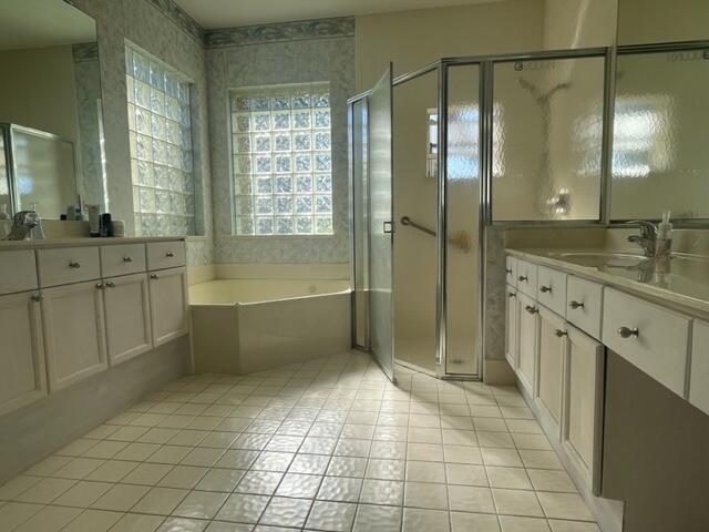 bathroom with tile patterned flooring, two vanities, a sink, a bath, and a stall shower