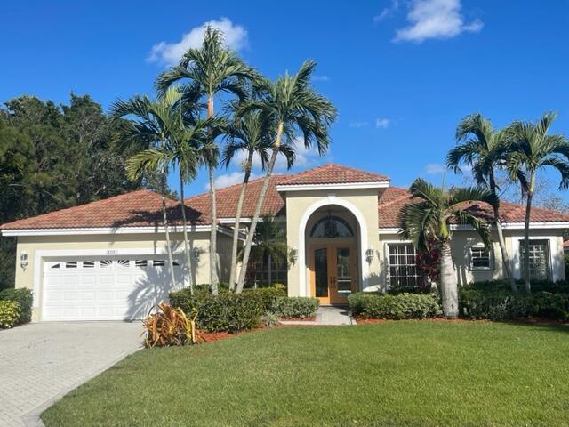 mediterranean / spanish house with a garage, driveway, a tiled roof, french doors, and a front lawn