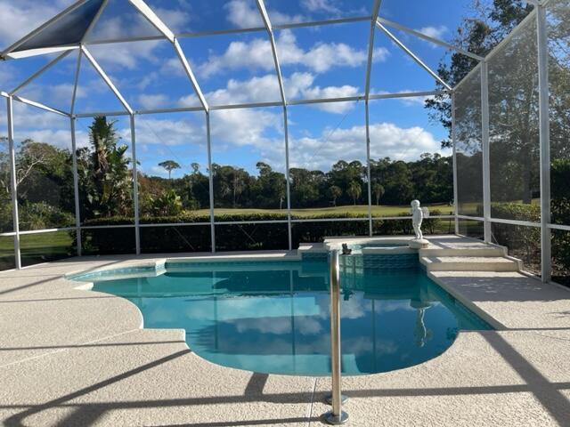 view of pool with glass enclosure, a pool with connected hot tub, and a patio