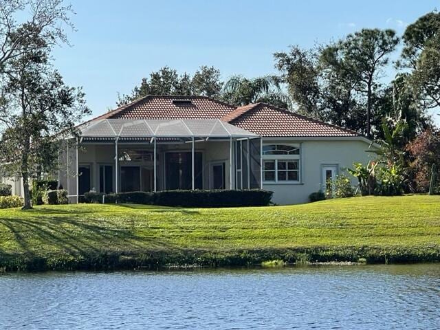 back of property featuring a lanai, a water view, a tile roof, a yard, and stucco siding