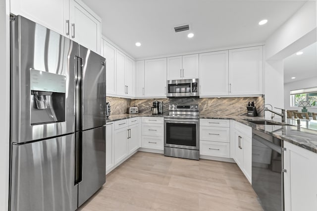 kitchen with appliances with stainless steel finishes, sink, light hardwood / wood-style flooring, dark stone countertops, and white cabinets