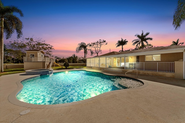 pool at dusk with an in ground hot tub and a patio area