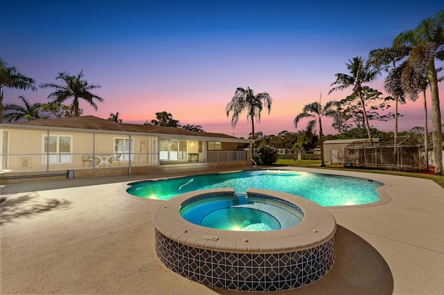 pool at dusk featuring an in ground hot tub and a patio