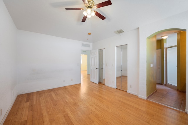 unfurnished bedroom featuring ceiling fan, light hardwood / wood-style floors, and two closets