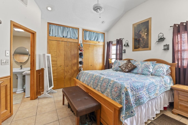 bedroom featuring ensuite bath, sink, light tile patterned floors, and vaulted ceiling