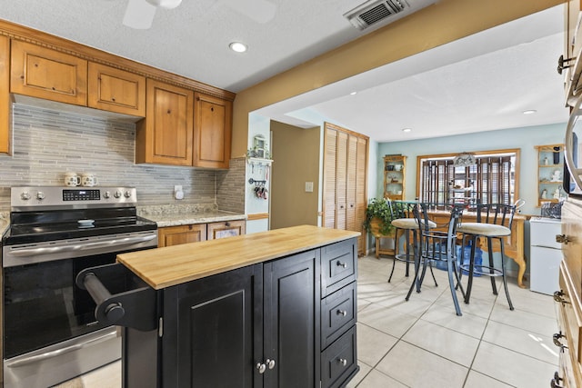 kitchen with stainless steel electric stove, decorative backsplash, ceiling fan, light tile patterned flooring, and butcher block counters