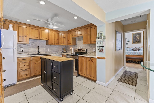 kitchen featuring ceiling fan, sink, a center island, white fridge, and stainless steel range with electric cooktop