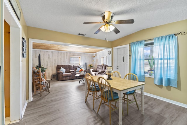 dining room with hardwood / wood-style floors, a textured ceiling, ceiling fan, and wooden walls