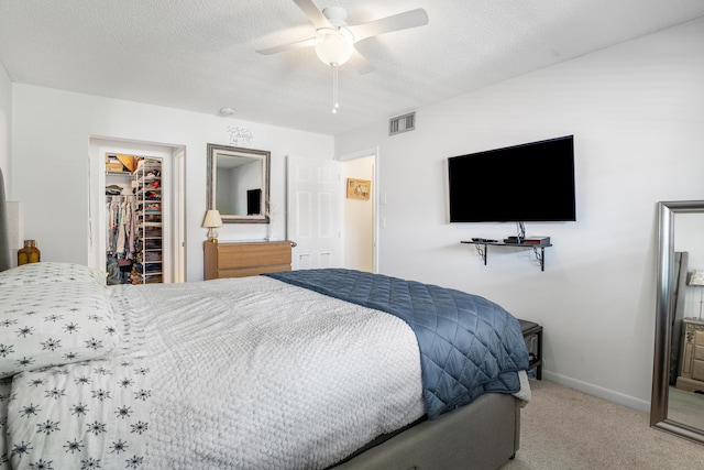 bedroom featuring light carpet, ceiling fan, a spacious closet, a textured ceiling, and a closet