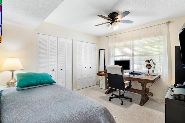 carpeted bedroom featuring a textured ceiling, ceiling fan, and two closets