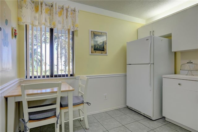 kitchen with white cabinets, white refrigerator, light tile patterned floors, and a textured ceiling