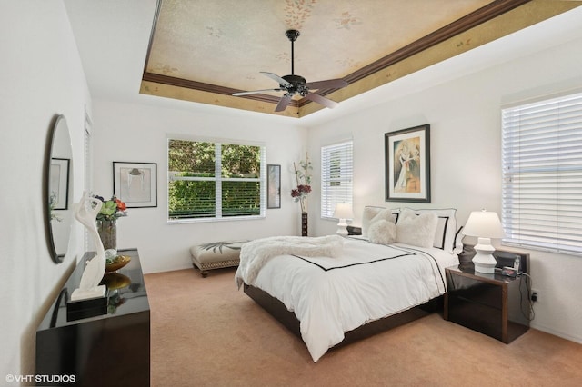 carpeted bedroom with a raised ceiling, ceiling fan, and crown molding