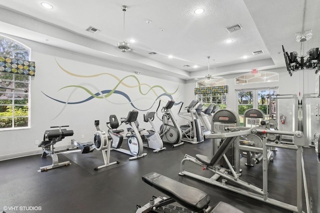 gym with a tray ceiling, ceiling fan, and a textured ceiling