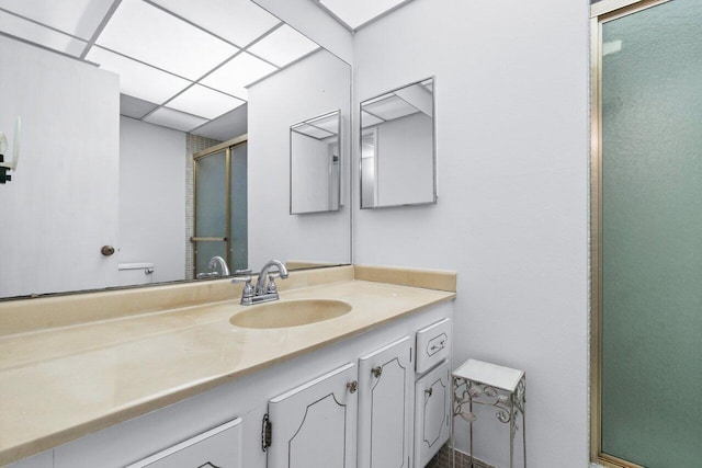 bathroom with a drop ceiling, a shower with door, and vanity