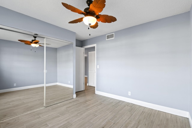 unfurnished bedroom with a textured ceiling, light wood-type flooring, a closet, and ceiling fan