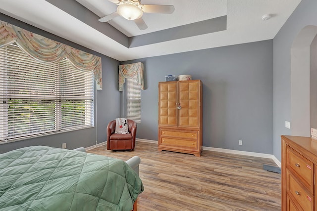 bedroom with ceiling fan, light hardwood / wood-style floors, and a tray ceiling