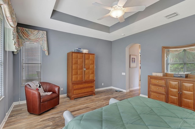 bedroom featuring ceiling fan, a raised ceiling, and light wood-type flooring