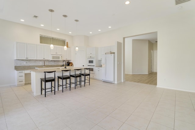 kitchen with white cabinetry, sink, hanging light fixtures, white appliances, and a kitchen island with sink