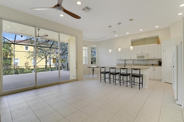 kitchen with hanging light fixtures, white cabinets, an island with sink, white appliances, and light tile patterned flooring