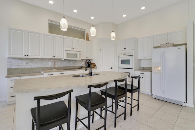 kitchen featuring white cabinets, decorative light fixtures, white appliances, and an island with sink