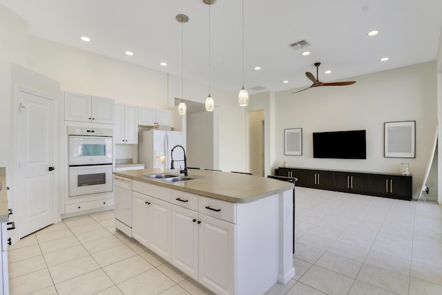 kitchen with white appliances, a kitchen island with sink, sink, pendant lighting, and white cabinetry